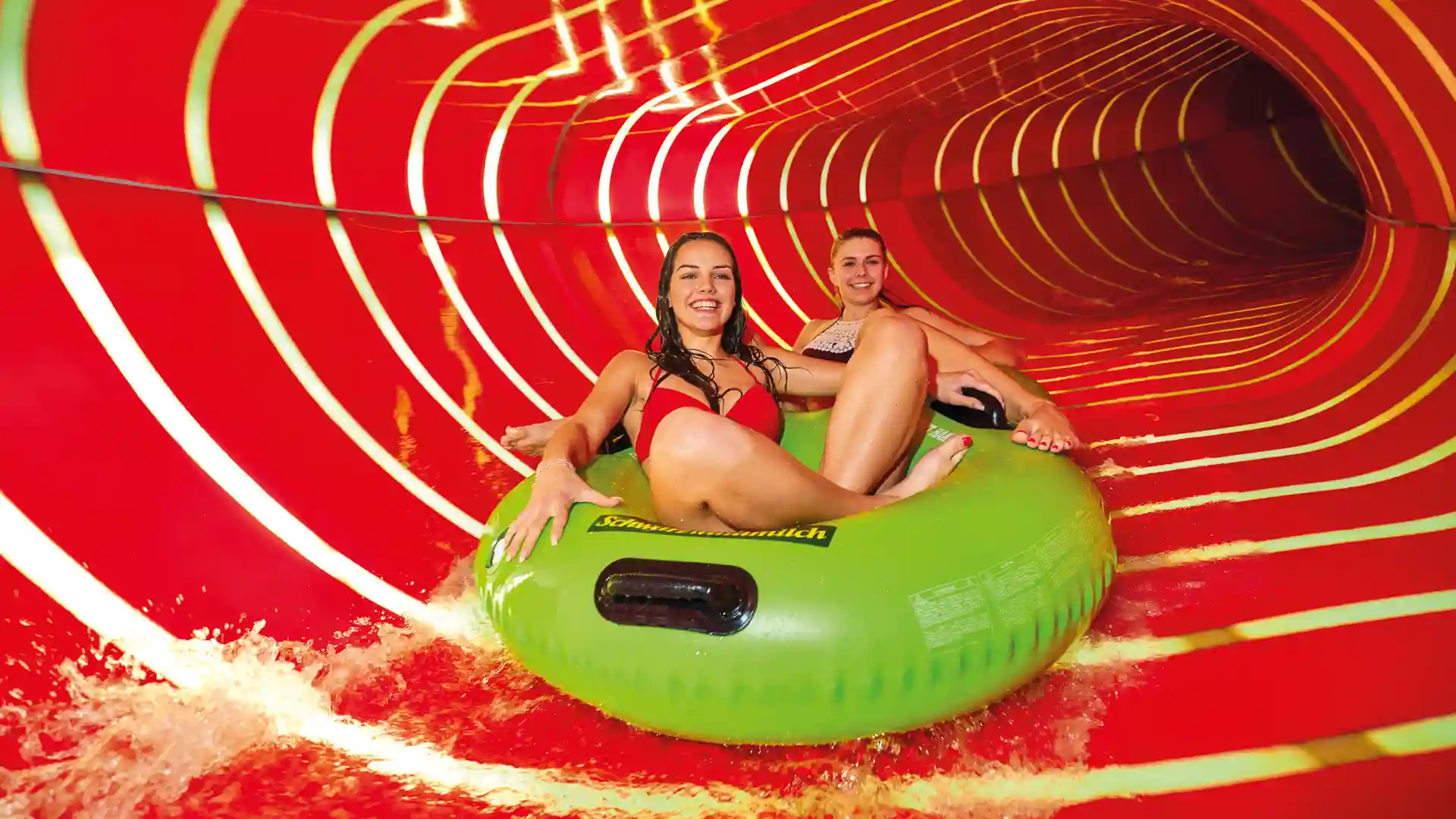 Zwei Frauen fahren auf grünem Reifen durch rot beleuchteten Family Twister.